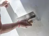 Ręka trzymająca kielnię wygładza białą ścianę.